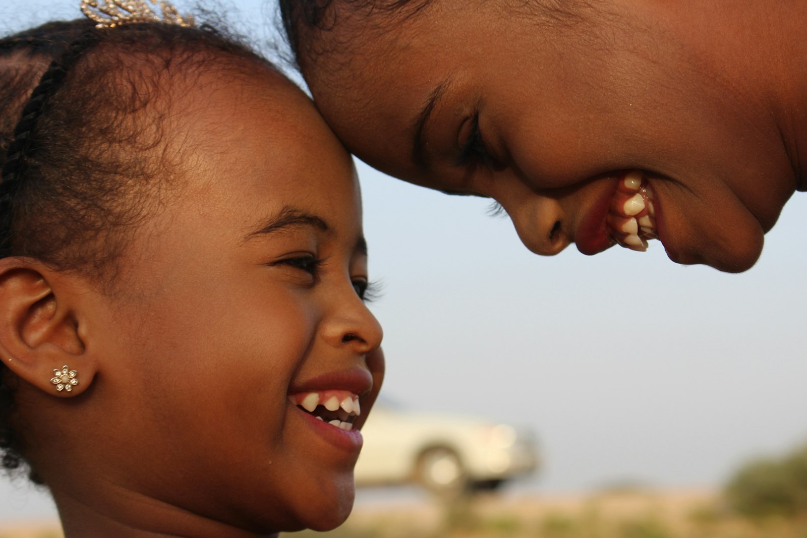 Two young children laughing together outdoors, foreheads touching